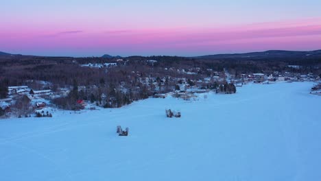 Luftrutsche-Entlang-Des-Ufers-Eines-Zugefrorenen-Sees-Nach-Einbruch-Der-Dunkelheit-Mit-Einem-Rosa-Himmel-An-Mehreren-Lagern-Vorbei