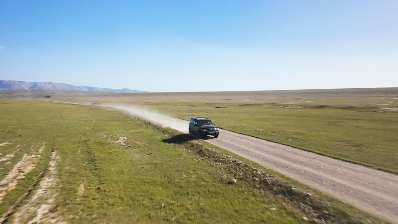 키르기스스탄의 켈-수 호수 근처 도로를 운전하는 suv의 회전하는 시네마틱 드론 샷