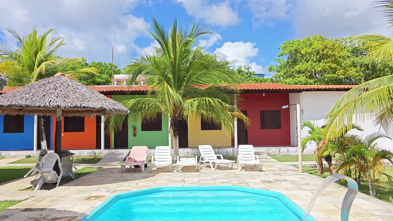 A man stands in front of a pool with a colorful building in the background