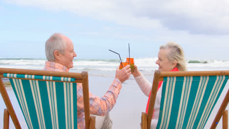 Side-view-of-old-caucasian-senior-couple-toasting-glasses-of-cocktail-at-beach-4k