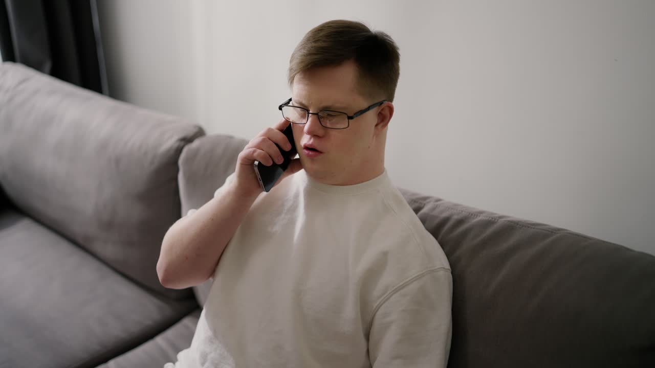 집에서 드폰을 사용하여 소파에 앉아 있는 잘생긴 다운 증후군 남자