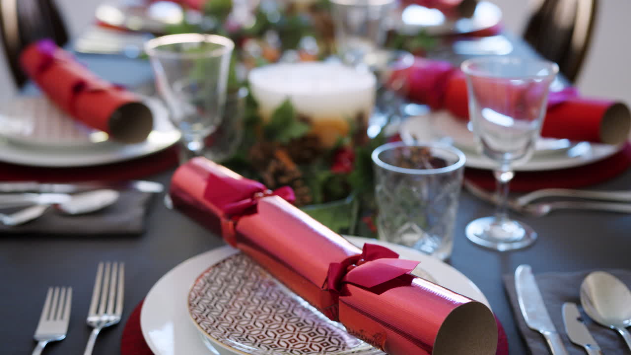 Tilt shot of a Christmas dinner table with seasonal decorations, crystal glasses and Christmas crackers on plates, elevated view