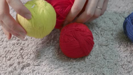 woman's hands put balls of thread for knitting of different colours on the floor.