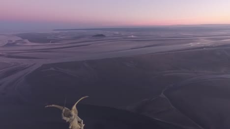 statue of saint michael on spire of mont saint michel abbey tower with bay in background at sunset