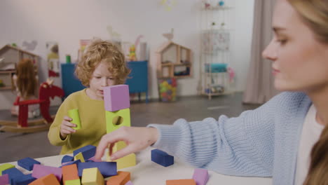 female teacher and blond little boy playing with foam building blocks in a montessori school 2