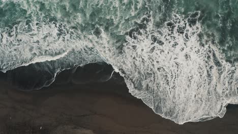 ozeanwellen mit schaumspritzern am schwarzen sandstrand von el paredon in guatemala - antenne von oben nach unten