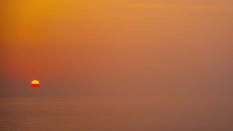 Sun-sets-behind-the-foggy-sea-horizon,-timelapse