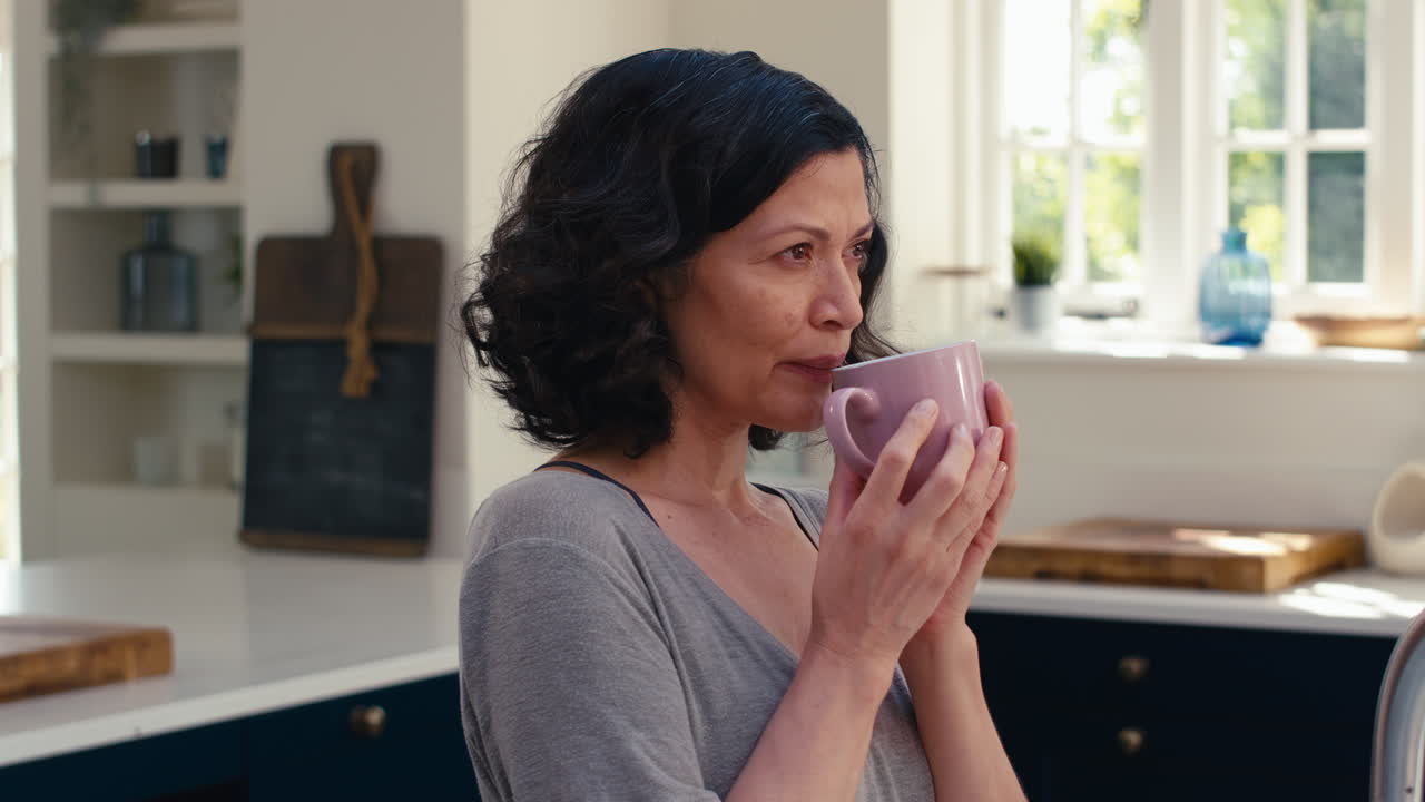 Close Up Of Smiling Mature Woman Standing In Kitchen Relaxing With Cup Of Coffee
