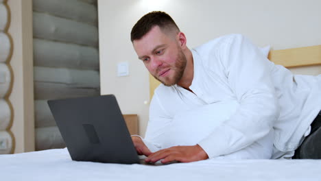 calm relaxed man half-lying on the bed. caucasian male uses his laptop working from home.
