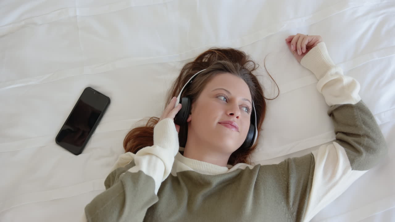 Relaxing on bed, woman listening to music with headphones, enjoying leisure time