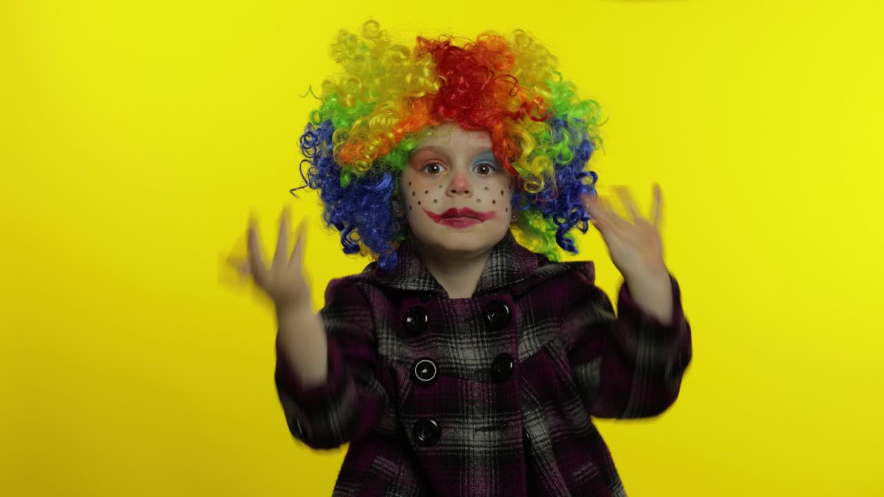 una pequeña niña payasa con una peluca colorida haciendo caras tontas, divirtiéndose, sonriendo, bailando. halloween