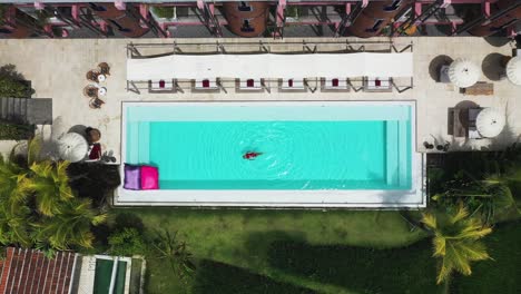 Natación-Femenina-Mirando-Al-Cielo-En-La-Piscina-Del-Hotel-Shore-Amora-Canggu-En-Bali,-Indonesia,-Tiro-De-Revelación-Aérea