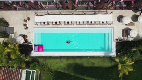 female swimming looking up at the sky at shore amora canggu hotel pool in bali, indonesia, aerial rising reveal shot