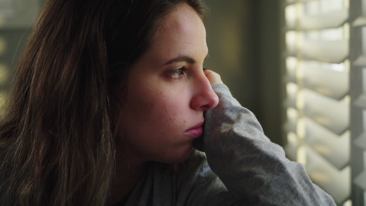 Mulher olha pela janela, ela está triste e solitária