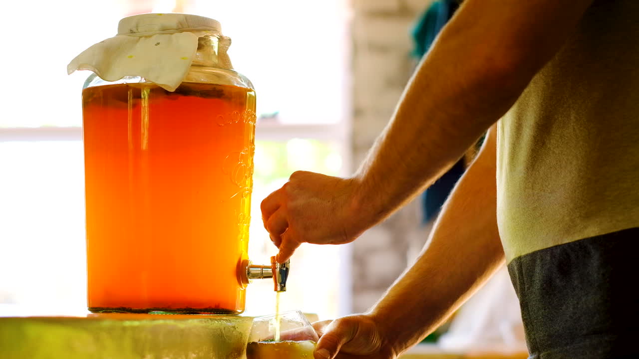 Uomo caucasico versa kombucha fermentata da un contenitore, bevanda probiotica