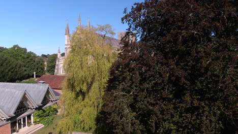 Rising-drone-shot-revealing-Winchester-Cathedral-from-behind-trees-during-Summer,-in-Hampshire,-UK