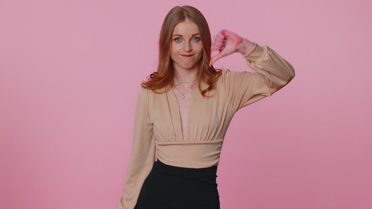 Upset girl in beige blouse showing thumbs down sign gesture disapproval dissatisfied dislike
