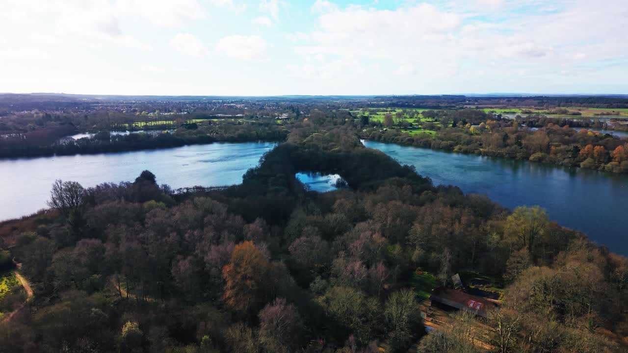 Drohnenaufnahme über einer bewaldeten Halbinsel, die sich in die Feuchtgebiete von Somerset erstreckt, mit umliegenden Seen und ferner Landschaft, die eine geschichtete Naturlandschaft bilden