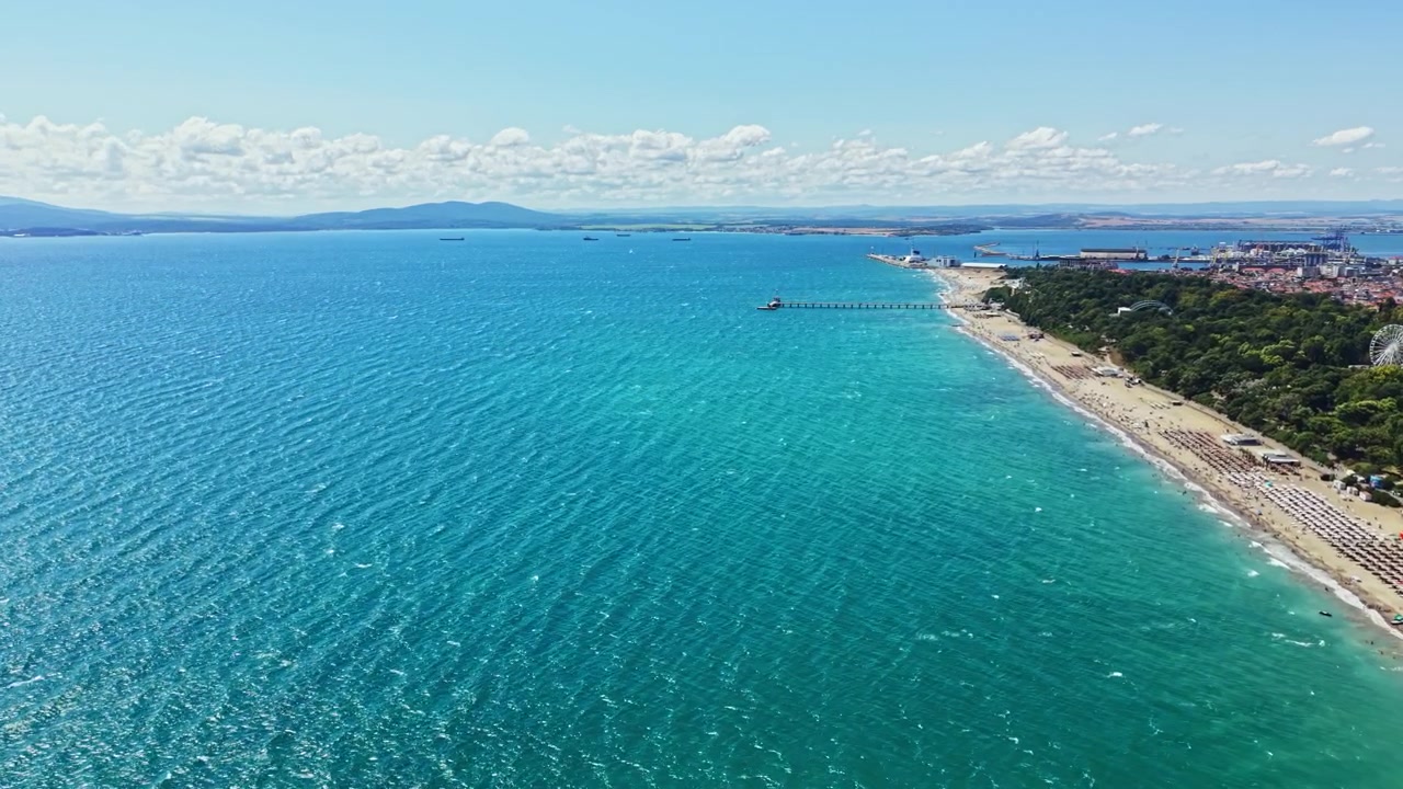 Mare blu cristallino incontra una spiaggia sabbiosa con moli distanti e una costa vivace in una giornata di sole d'estate
