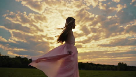 girl in pink dress dancing in field at sunset