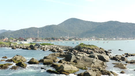 Vista-Cinemática-Aérea-Rocas-Costa-Y-Barcos,-Praia-Armacao,-Florianópolis,-Santa-Catarina,-Brasil