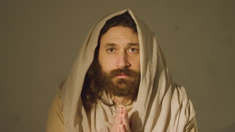 Portrait-Of-Man-Wearing-Robes-With-Long-Hair-And-Beard-Representing-Figure-Of-Jesus-Christ-Putting-Hands-Together-In-Prayer-