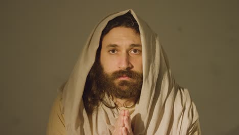 retrato de un hombre vestido con túnicas con cabello largo y barba que representa la figura de jesucristo poniendo las manos juntas en oración