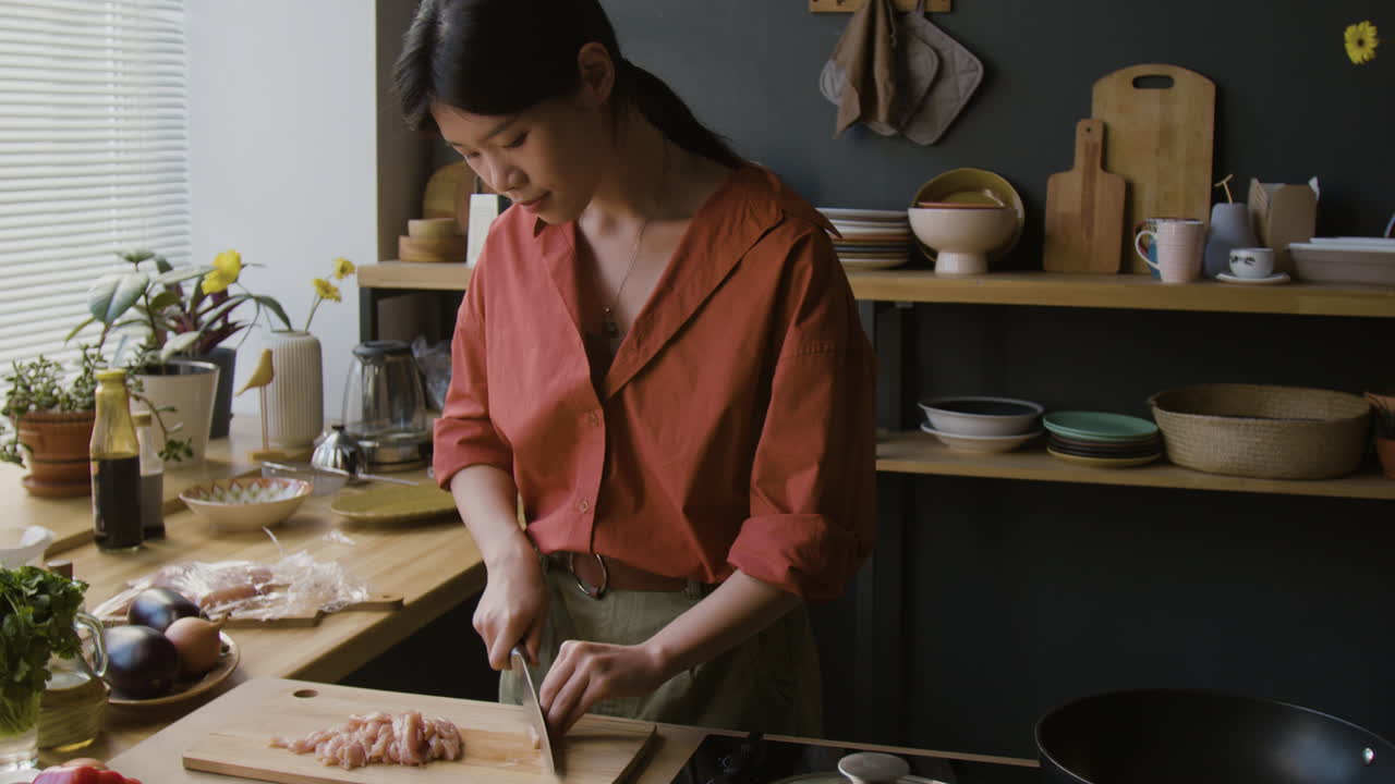 Young Asian woman chopping chicken in a home kitchen
