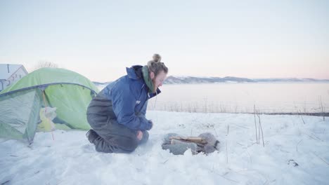 guy blowing hard firewood on the campfire during camping trip at wintertime