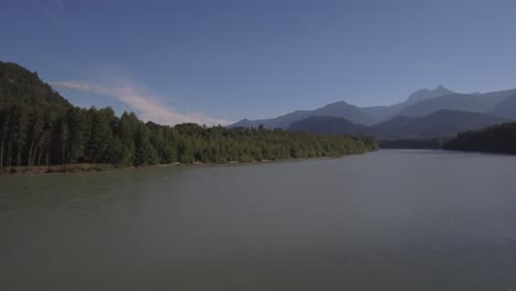 4K-Drone-footage-flying-over-a-large-river-with-blue-water,-mountains-and-forest