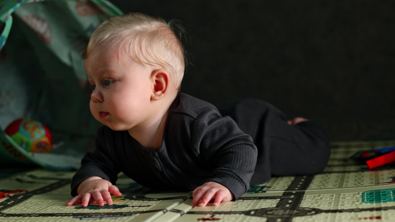 Un neonato impara a tenere su la testa mentre è sdraiato sul pavimento. Un bambino piccolo gioca sul pavimento di casa. Il bambino gioca da solo a casa. Sviluppo infantile.