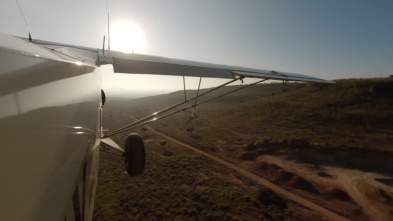 Piccolo aereo in vista laterale sopra arbusti, strada e colline