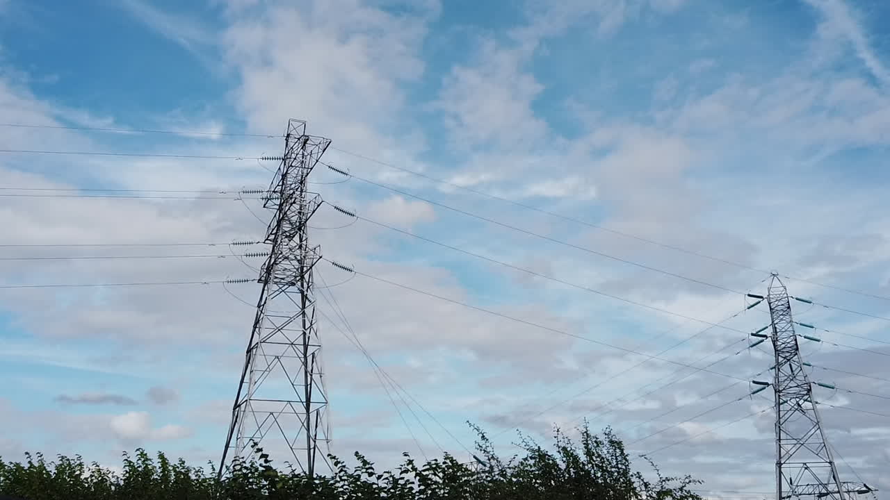 Electricity pylons standing tall against a blue sky with fluffy clouds floating by
