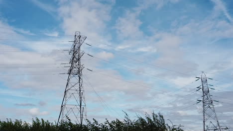 Torres-De-Alta-Tensión-De-Pie-Contra-Un-Cielo-Azul-Con-Nubes-Esponjosas-Flotando-Por