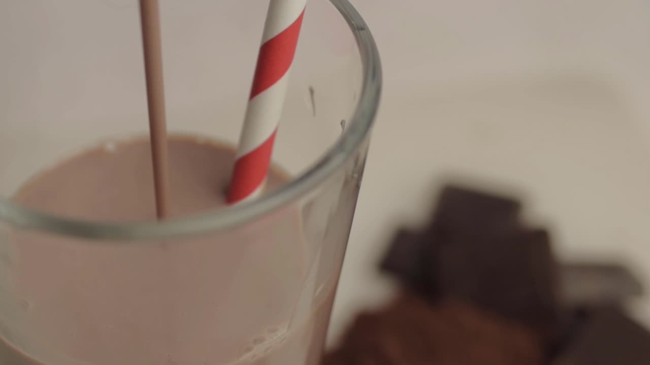 Versare un milkshake al cioccolato in un bicchiere con cannuccia, primo piano