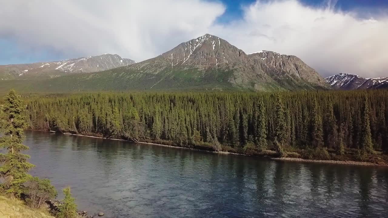 hermoso vuelo panorámico a lo largo del borde del río takhini con árboles verdes y montañas en el fondo en un día soleado, yukon, canadá, vista aérea lateral