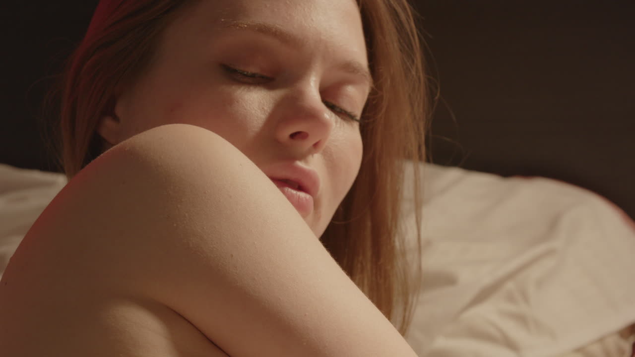 Una bella donna a seno scoperto posa sensualmente a letto e gira la testa al rallentatore.