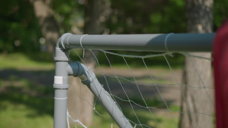 a close-up view of a soccer ball as it hits the net, scoring a goal, the goalkeeper's right hand is seen reaching for the ball, attempting to save it after it has already entered the net