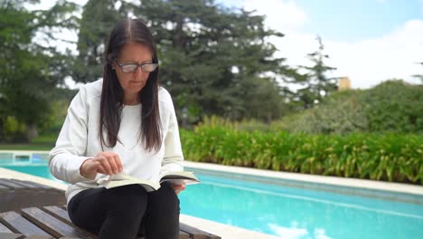 adult woman with eyeglasses reading book and sitting by the poolside