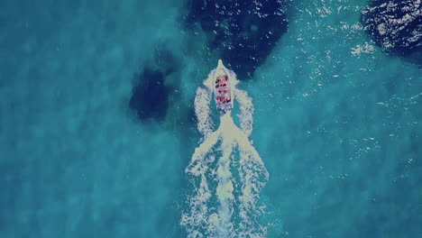 Top-down-aerial-overhead-small-boat-driving-on-bright-blue-ocean-water