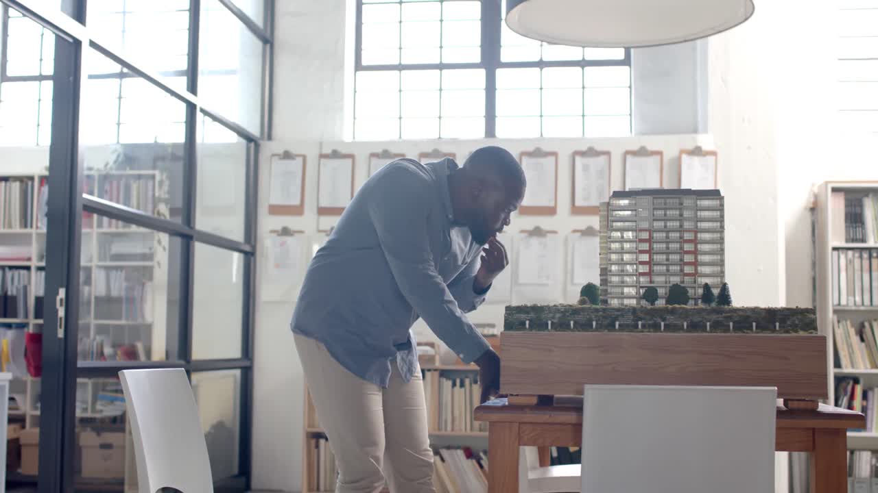 Empresário casual afro-americano focado inspecionando um modelo de cidade no escritório, em câmera lenta.
