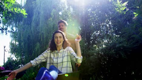 Man-carrying-woman-in-wheelbarrow-in-garden