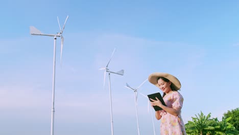 asian young woman using a digital tablet in the field in the background wind power production turbines