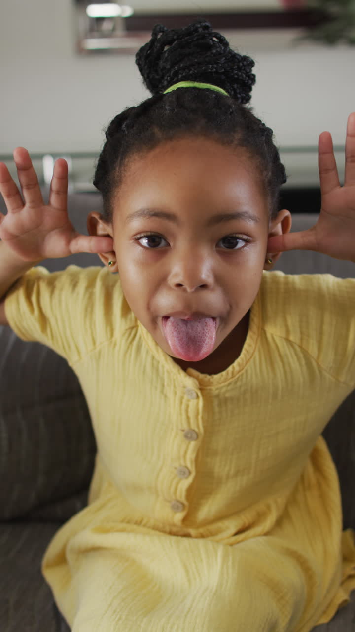 вертикальный видеопортрет счастливой афроамериканской девушки, делающей смешное лицо и высунувшей язык.