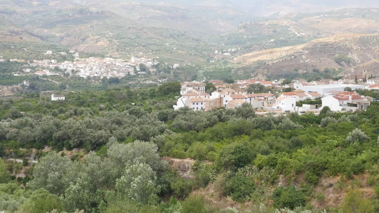 Vista di Melegís circondata da una fitta vegetazione di ulivi e agrumi. Il paesaggio mostra l'architettura rurale integrata nell'ambiente naturale della Valle di Lecrín in Andalusia.