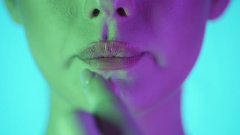disparo estático en cámara lenta de los labios de una hermosa mujer joven mientras ella pone un chicle dulce y delicioso en su boca y comienza a masticar frente al fondo turquesa con contraste púrpura verde en la cara