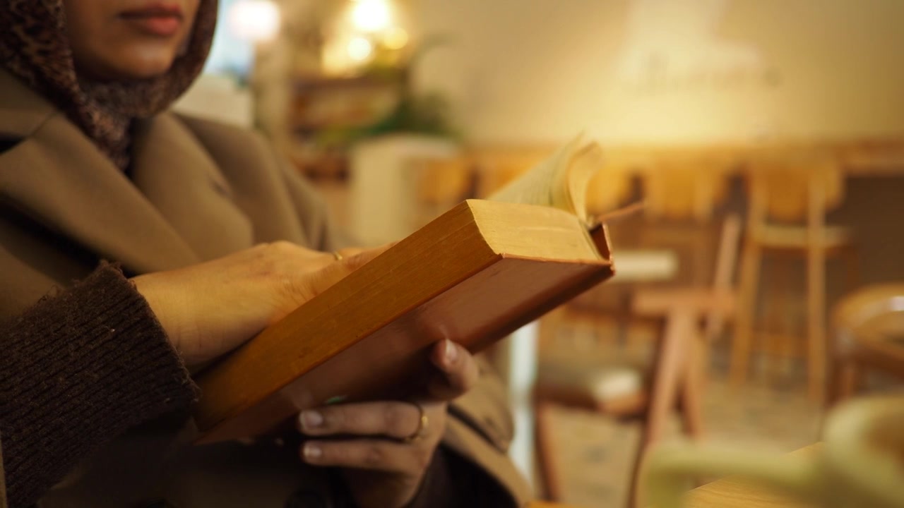 Donna con hijab che legge un libro in un caffè accogliente