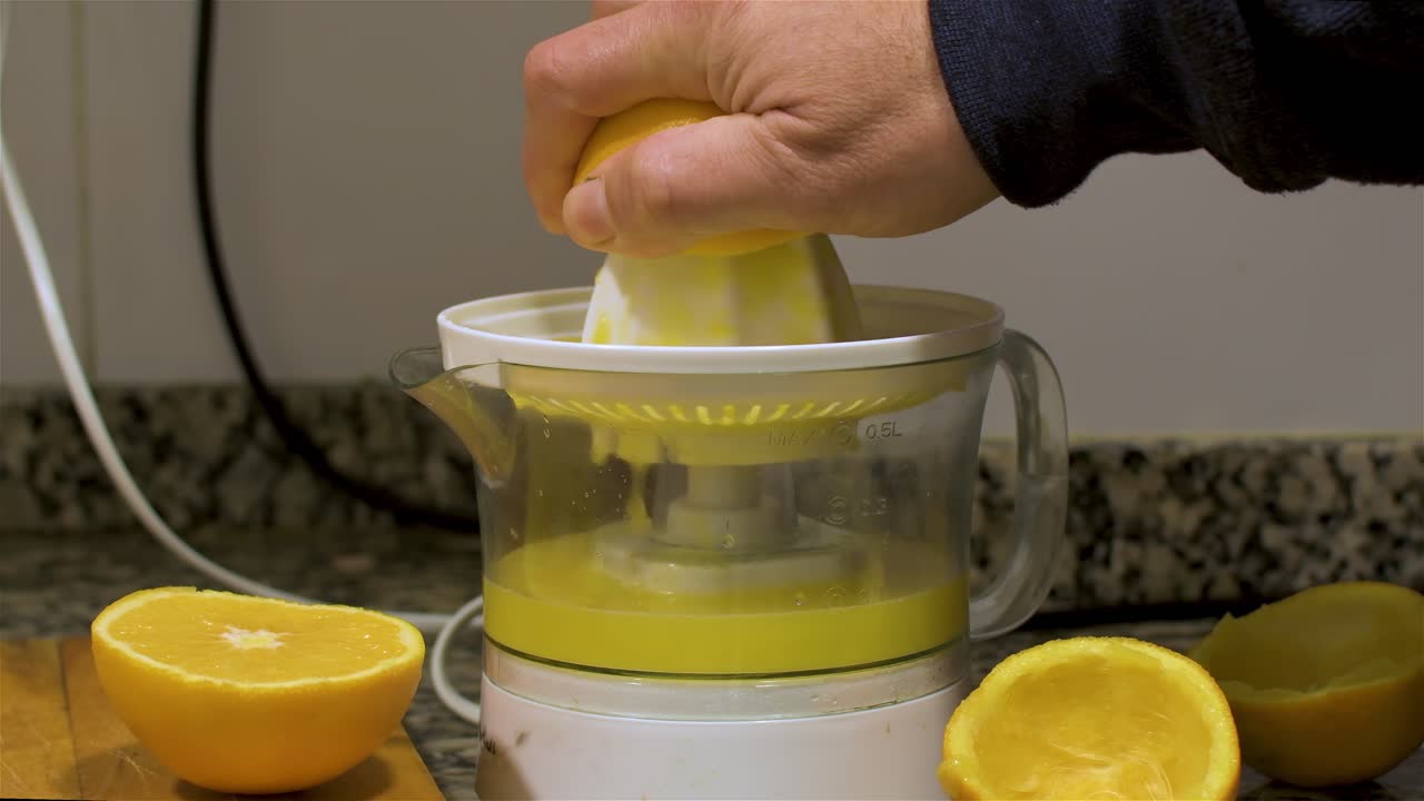 부엌에 있는 오렌지 과즙기에 오렌지 반쪽을 쥐고 있는 손의 모습