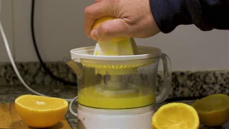 view of a hand squeezing half an orange in a orange juicer in the kitchen