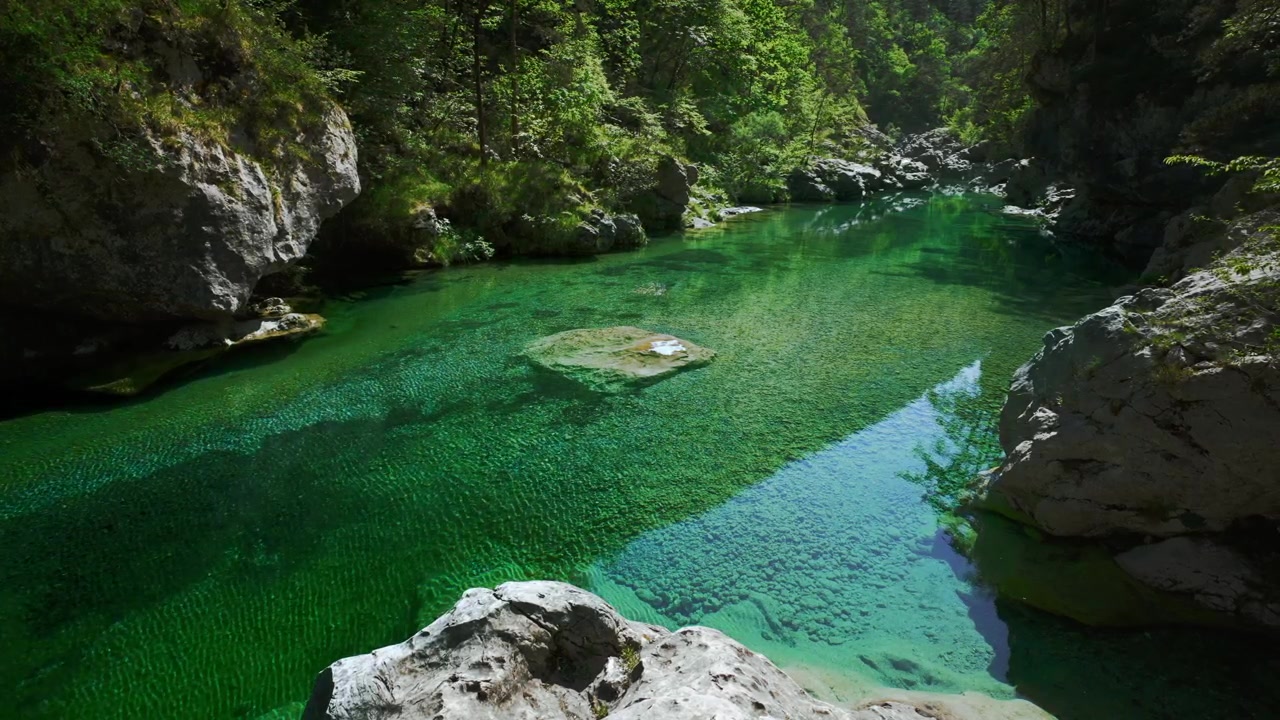 Ruscello di acqua turchese incontaminata che scorre dolcemente su ciottoli di fiume bianchi e lisci alle Pozze Smeraldine